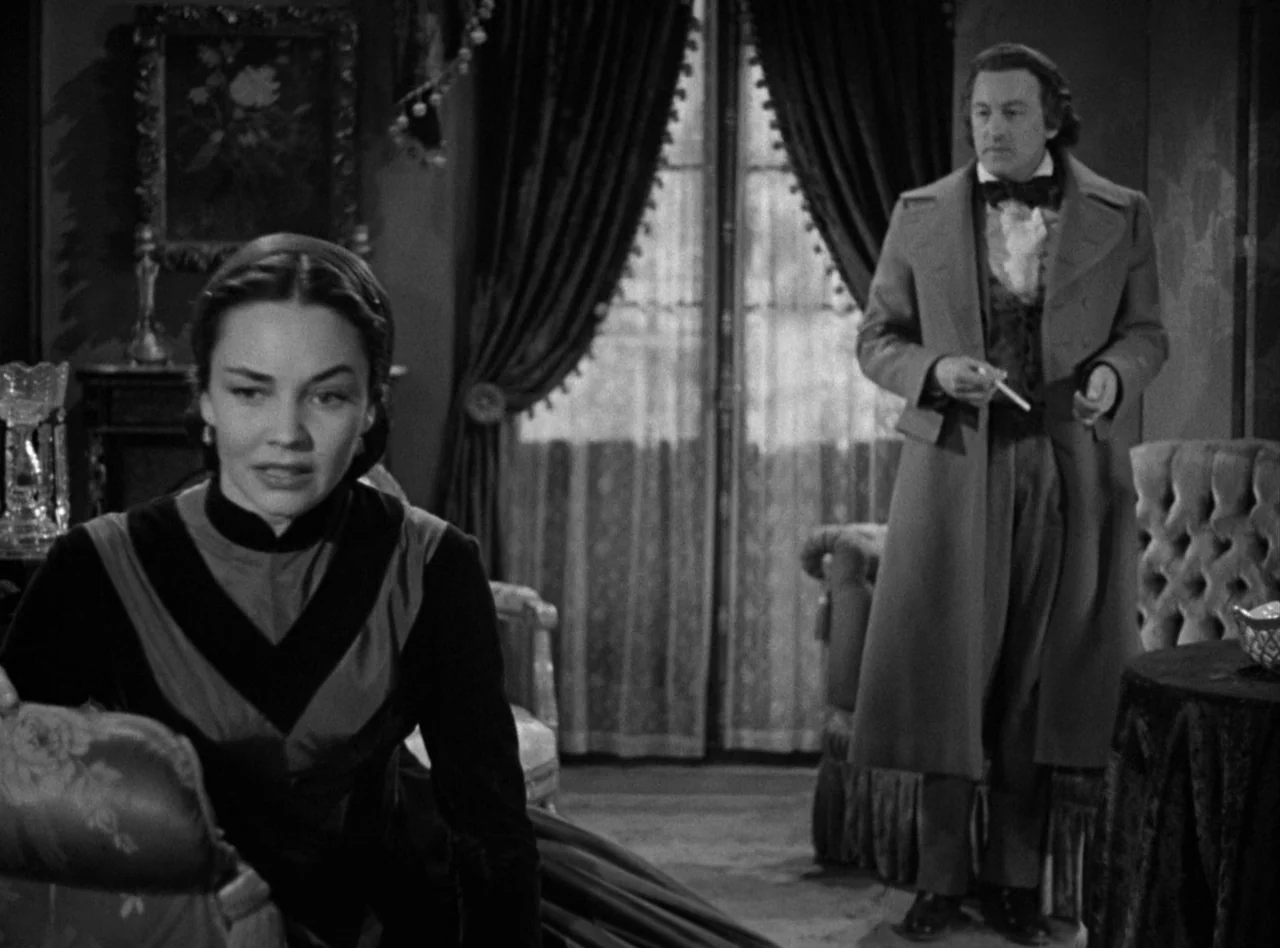 Madame Bovary (1949) movie still: medium — An opulent parlor with heavy floor-length curtains and ornate period furniture arranged throughout. A…
