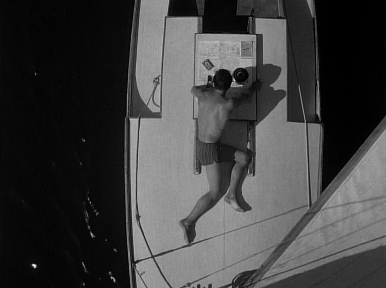 Knife In The Water (1962) movie still: wide — The deck of a sailboat at night is illuminated by a single overhead light. A man lies prone on the…