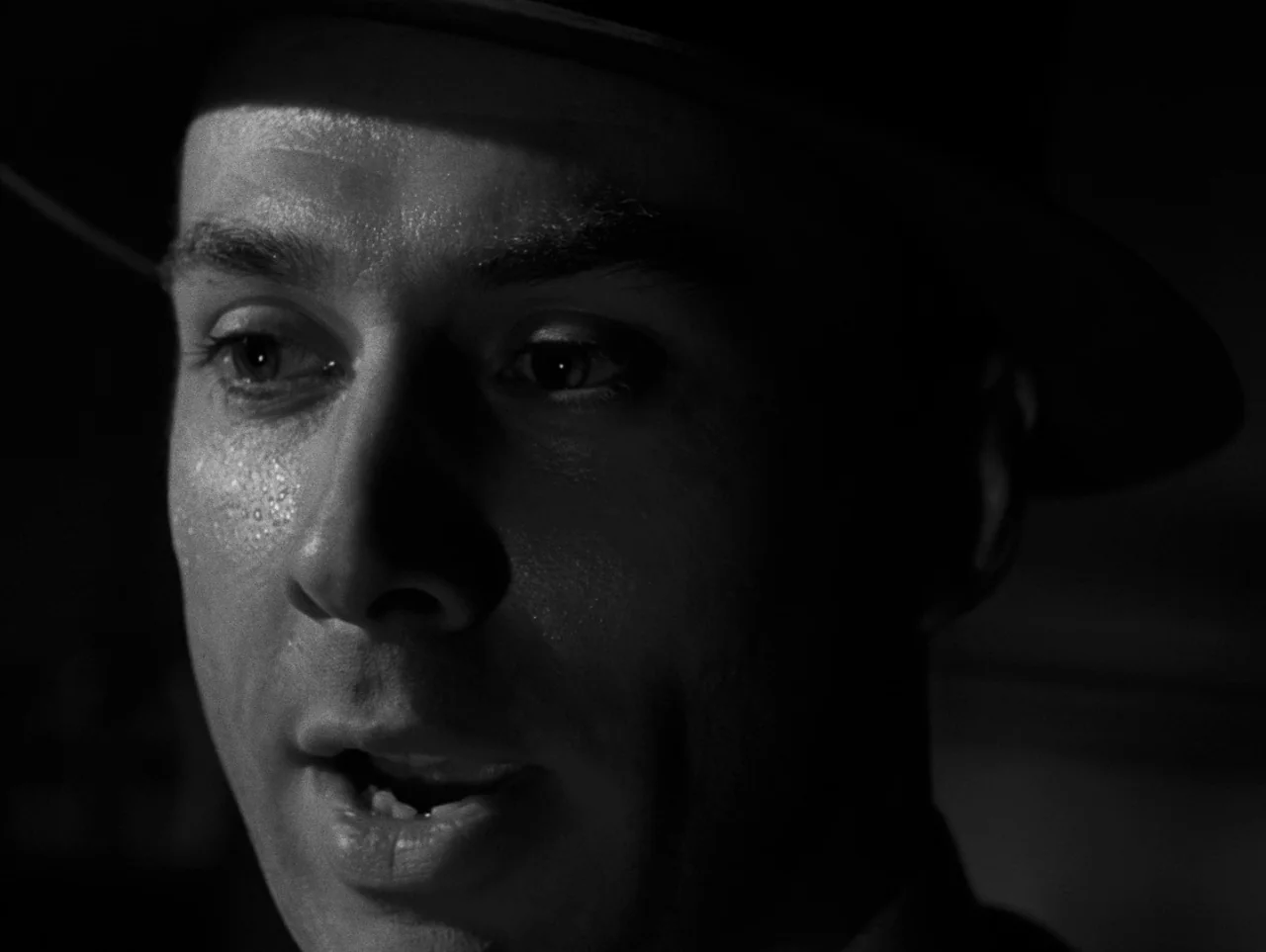 Pickup on South Street (1953) movie still: closeup — The frame captures the upper half of a man's face in deep shadow. He stares with his mouth…