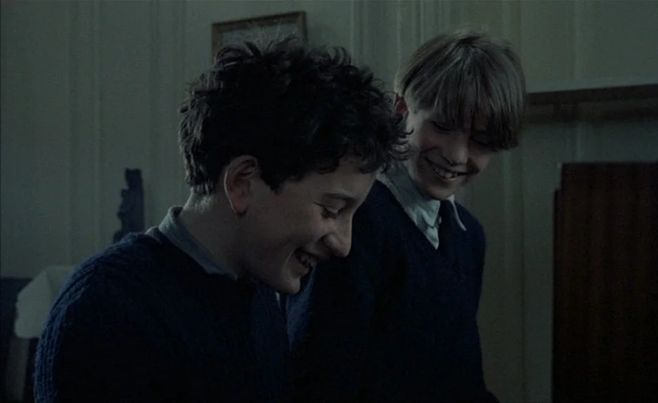 Au Revoir Les Enfants (1987) movie still: medium — A dimly lit room with muted walls and minimal furniture suggests a period institutional setting.…