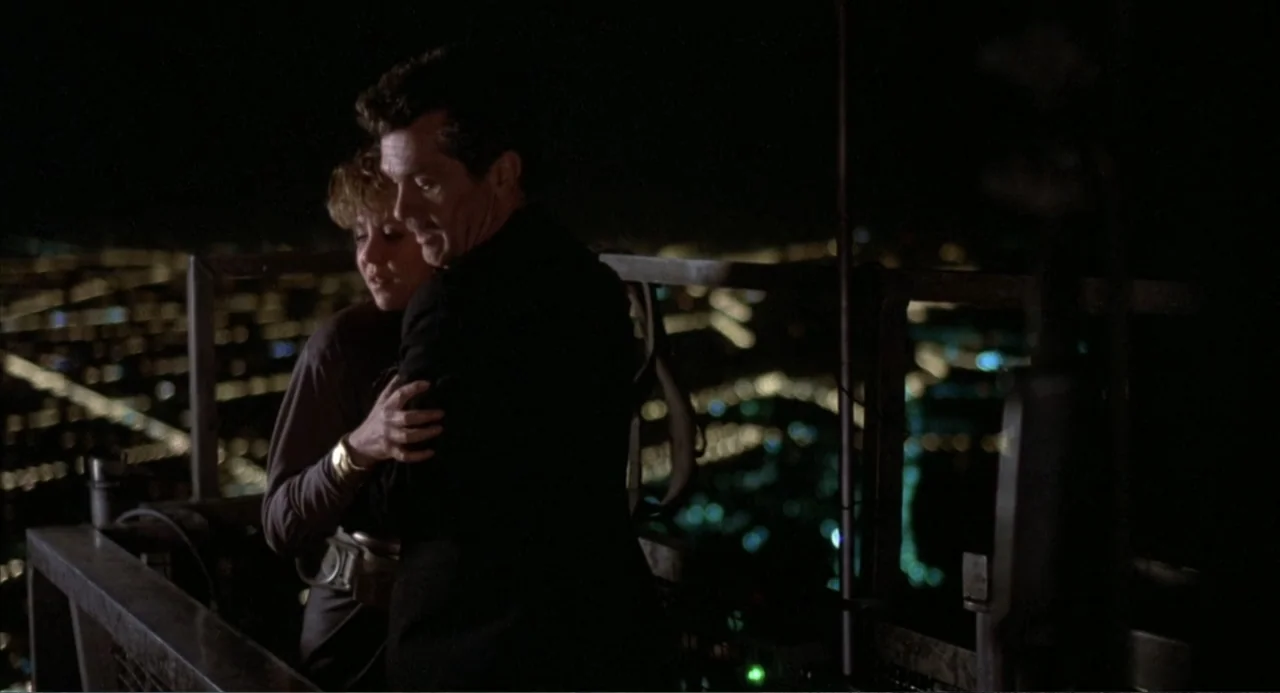 Poltergeist III (1988) movie still: medium — A dark outdoor platform overlooks a distant city blurred into bokeh lights at night. A man and a woman…