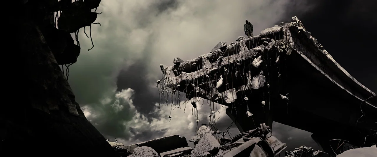 The Book of Eli (2010) movie still: wide — A decimated concrete overpass with exposed rebar towers over a landscape of gray rubble. A lone…