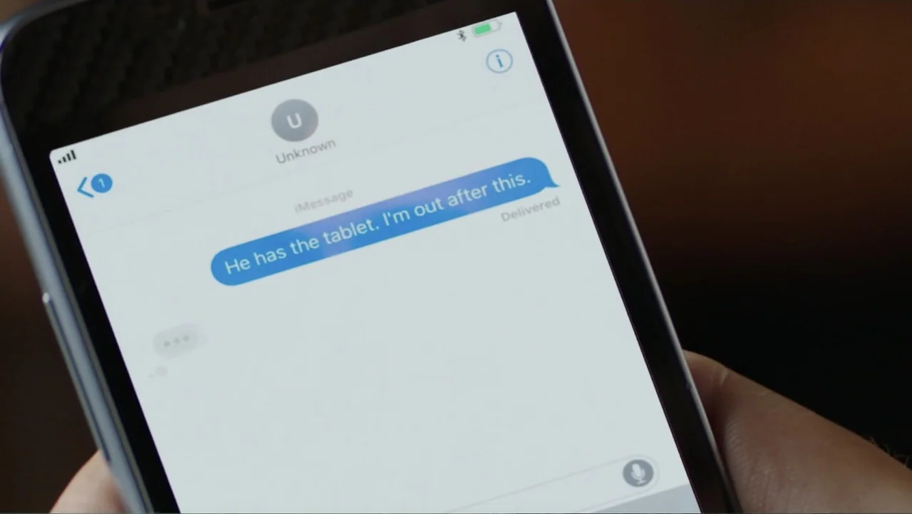 Skyscraper (2018) movie still: closeup — A close-up view shows a smartphone screen displaying a text message conversation. The message states, 'He…