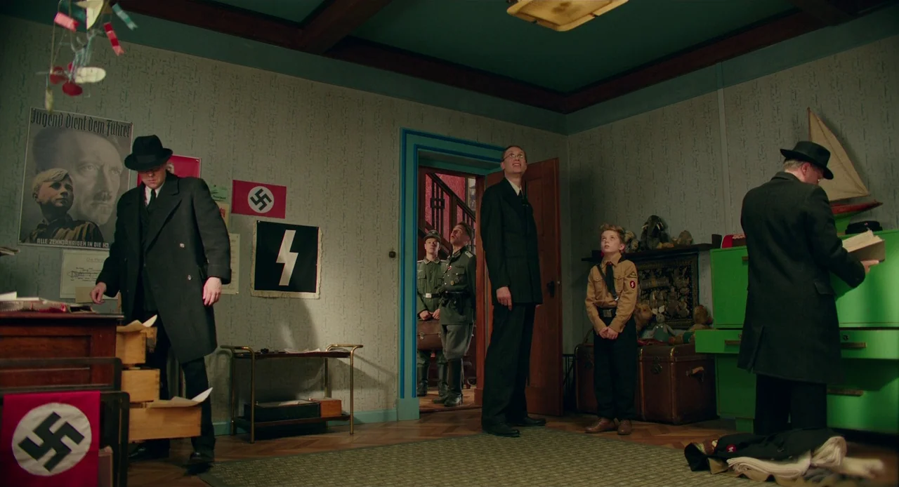 Jojo Rabbit (2019) movie still: wide — A 1940s child's bedroom features pale green wallpaper, a green desk, and political propaganda. Several men in…