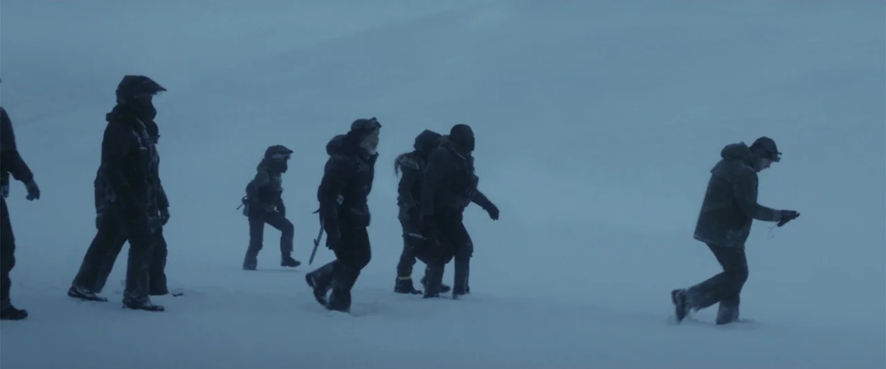 The Tomorrow War (2021) movie still: wide — A group of people wearing heavy winter gear traverses a vast, featureless snow-covered landscape. A…