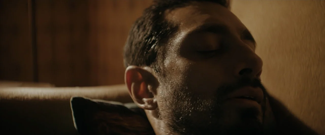 Encounter (2018) movie still: closeup — An interior space features a man resting his head against a plain wall. The subject keeps his eyes closed…