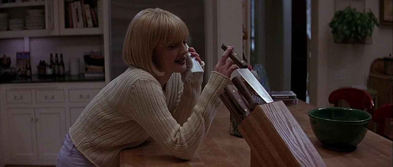 Scream (1996) movie still: medium — A residential kitchen features white cabinetry, a wooden countertop, and a wooden knife block. A young woman…