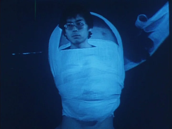 A Tale of Smallpox (1975) movie still: medium — A man stands in an undifferentiated dark space with no visible background architecture. He is…