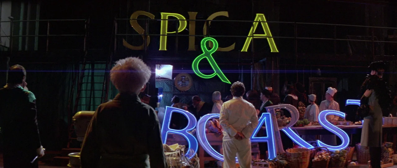 The Cook, The Thief, His Wife & Her Lover (1989) movie still: wide — An interior market stall features large neon signs reading SPICA & BOARS on…