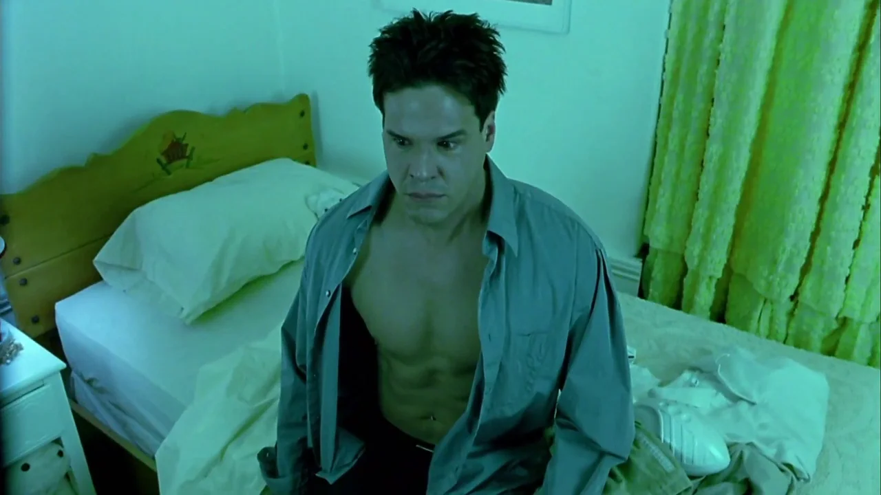 Hellraiser: Inferno (2000) movie still: medium — A man sits on a bed in a room with green-tinted walls and light curtains. The man in an open shirt…