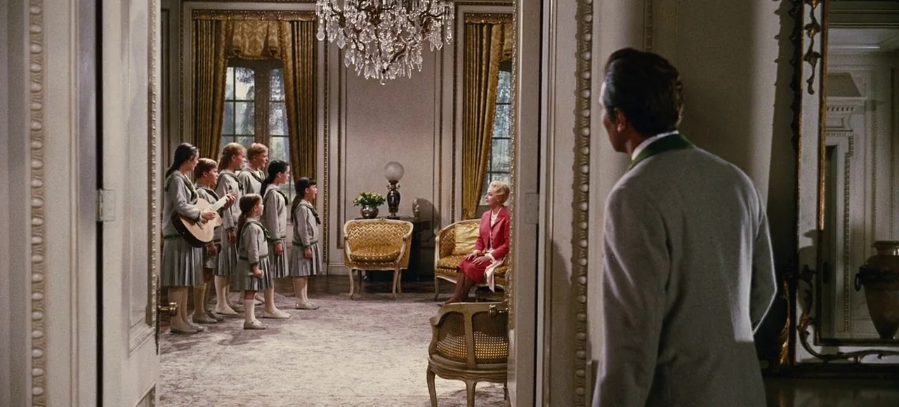 The Sound of Music (1965) movie still: wide — A formal, high-ceilinged parlor with crystal chandelier and gold-upholstered chairs faces a wide…