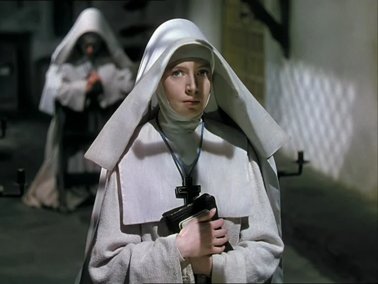 Black Narcissus (1947) movie still: medium — A stone corridor in a nunnery with white walls and a visible second nun. A young nun in white habits…