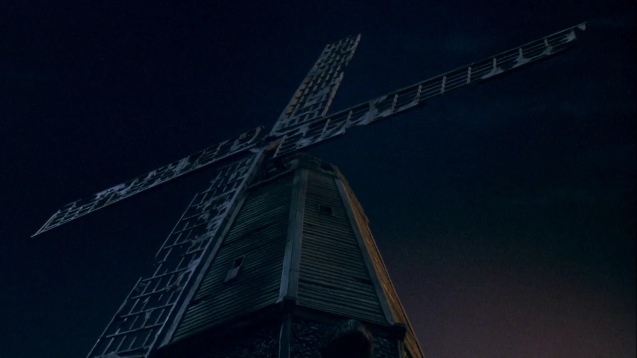 Army of Darkness (1992) movie still: wide — A dark wooden windmill stands against a clear night sky. The structure features worn wood siding and…