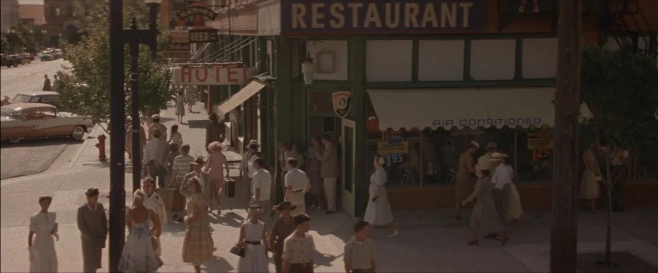 This Boy's Life (1993) movie still: wide — A bustling 1950s small-town sidewalk is lined with a hotel and a restaurant. Pedestrians dressed in…