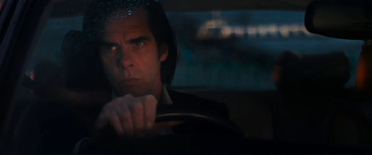 20,000 Days on Earth (2014) movie still: closeup — The interior of a car at night with rain droplets visible on the glass. A man sits in the…
