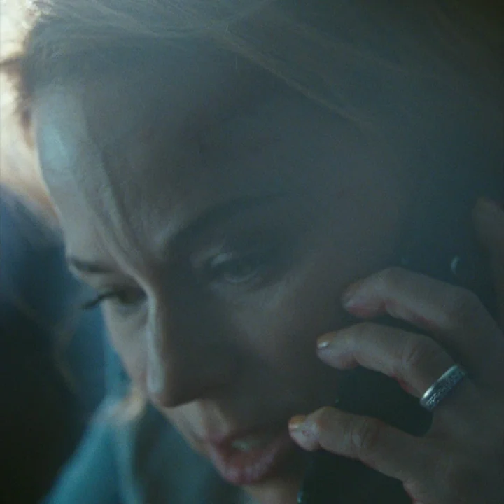 Mommy (2014) movie still: closeup — The interior of a vehicle is dark, with blue tones from a mobile device. A woman holds her phone to her ear…