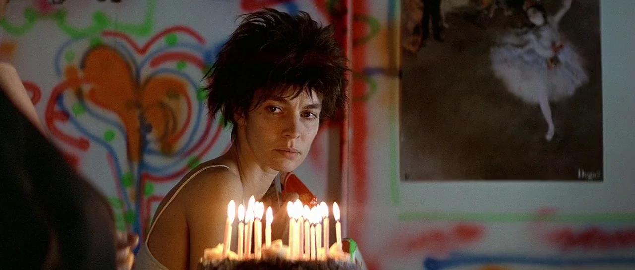 Nikita (1990) movie still: medium — A wall covered in colorful spray-painted graffiti and a ballerina poster. A woman with short hair stares into…
