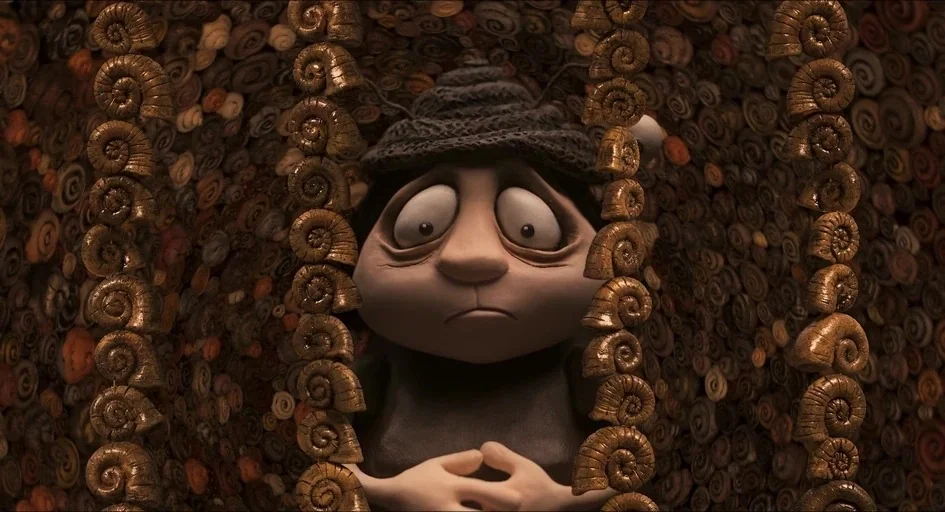 Memoir of a Snail (2024) movie still: closeup — The interior of a wall covered in many small spiral-shaped snail shells. A small creature with large…