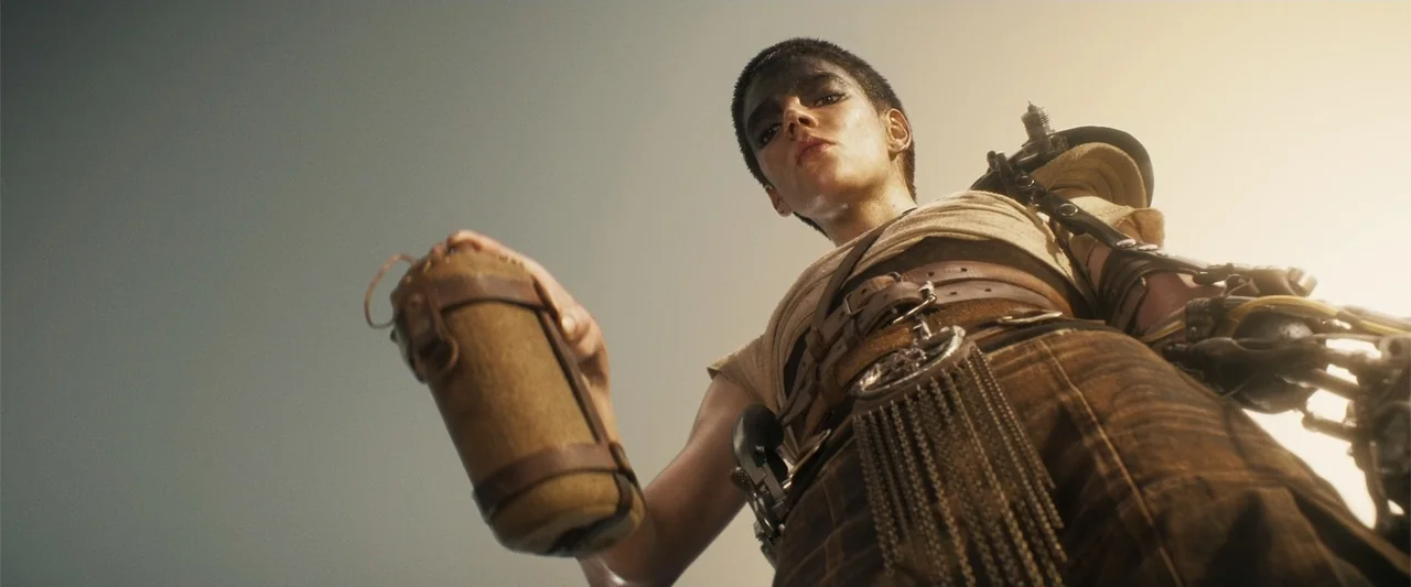 Furiosa: A Mad Max Saga (2024) movie still: medium — An arid, sun-bleached desert landscape under a clear bright sky. A person with short hair and a…