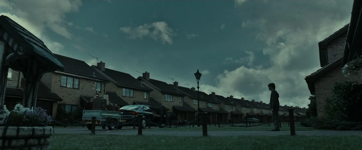 Harry Potter & The Deathly Hallows Part 1 (2010) movie still: wide — A row of identical suburban brick houses stretches along a quiet street under…