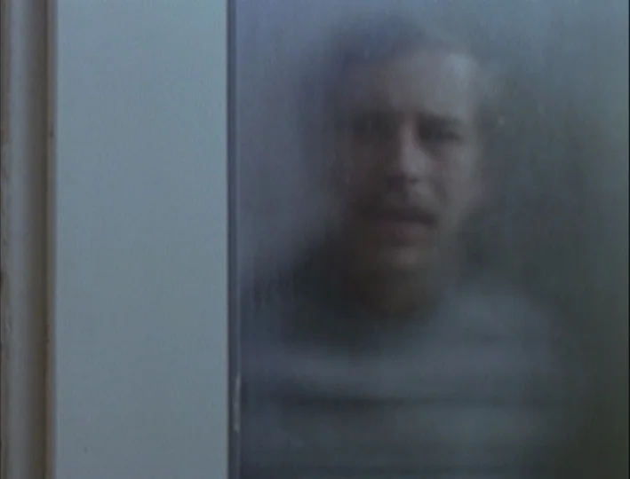 Camera Buff (1979) movie still: closeup — A man stands behind a fogged glass panel or door. His face is partially obscured by the condensation on…