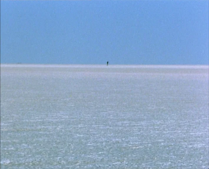 Fata Morgana (1971) movie still: establishing — A vast, flat expanse of white salt stretches to a distant, hazy blue horizon. A single, tiny dark…