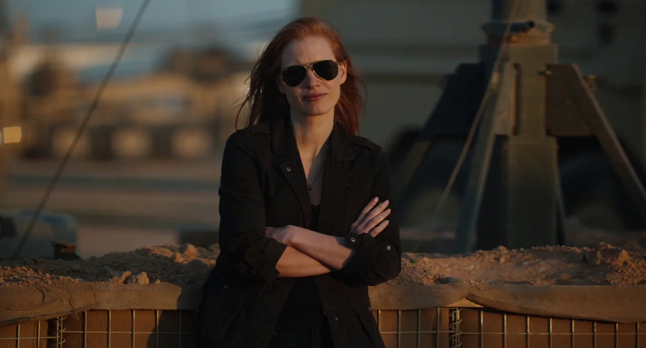 Zero Dark Thirty (2012) movie still: medium — A military compound with sand-filled barriers and heavy equipment visible in the background. A woman…
