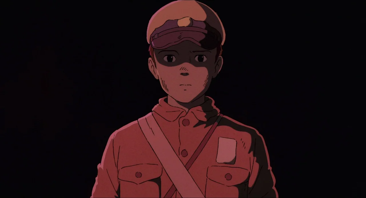 Grave of the Fireflies (1988) movie still: medium — A teenage boy stands in complete darkness. He wears a simple red uniform and a matching…