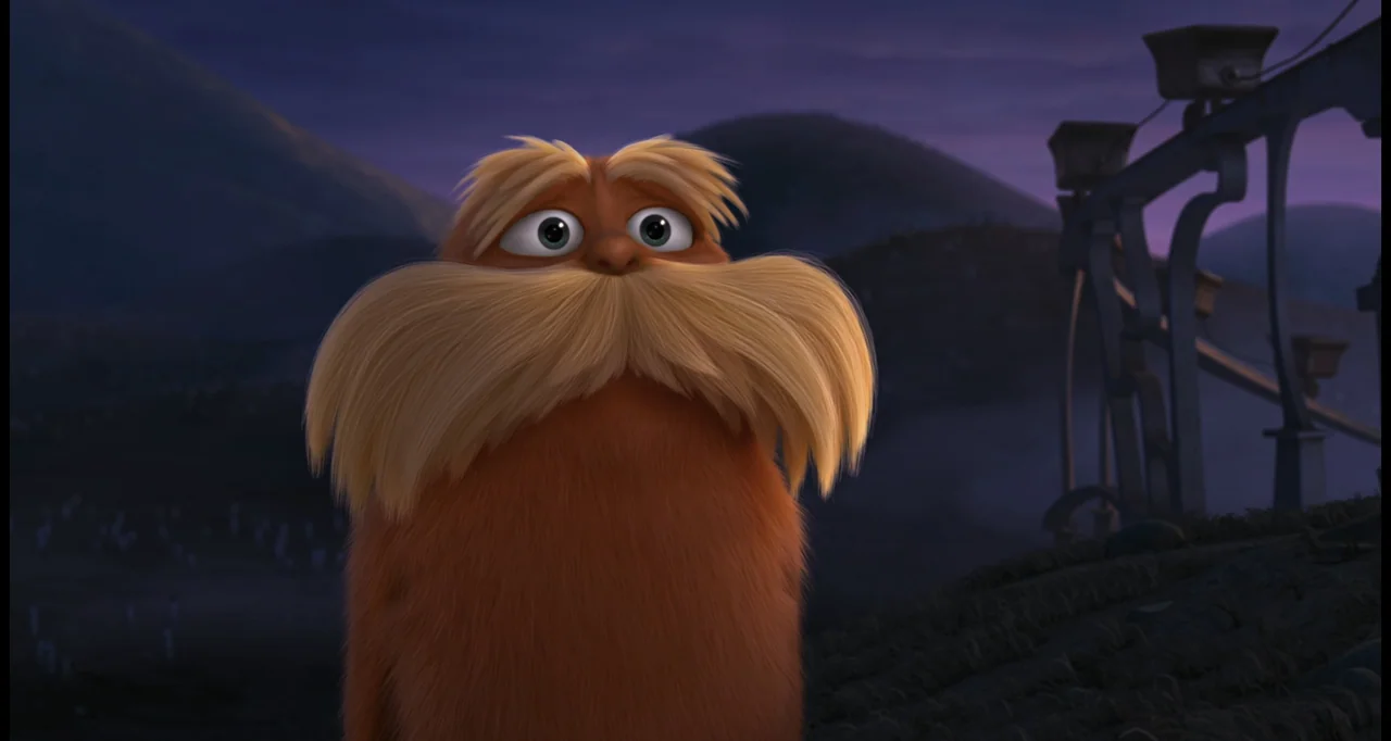 The Lorax (2012) movie still: closeup — A furry orange creature with a large yellow mustache stands in a hilly landscape. The background features…
