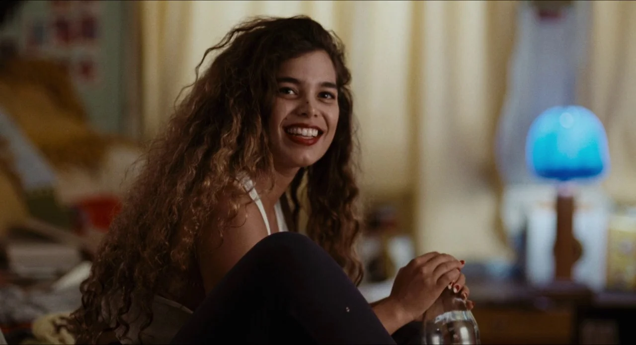 Deep Cover (1992) movie still: medium — A cluttered interior space with yellow curtains and a blue light in the background. A young woman with long…