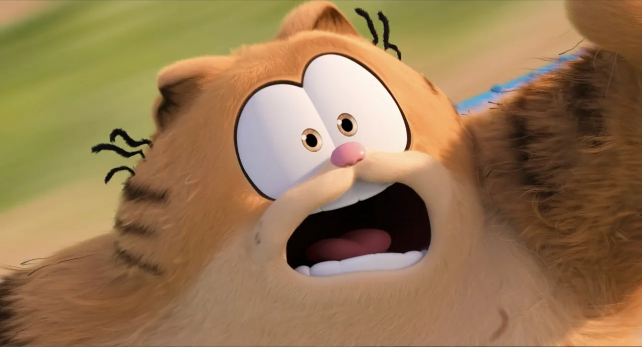 The Garfield Movie (2024) movie still: closeup — A close-up of an orange cat character with large white eyes outdoors. The cat has a startled…