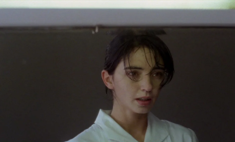 Casa De Lava (1994) movie still: closeup — A woman stands in a dimly lit, narrow corridor with plain dark walls. She looks slightly away from the…