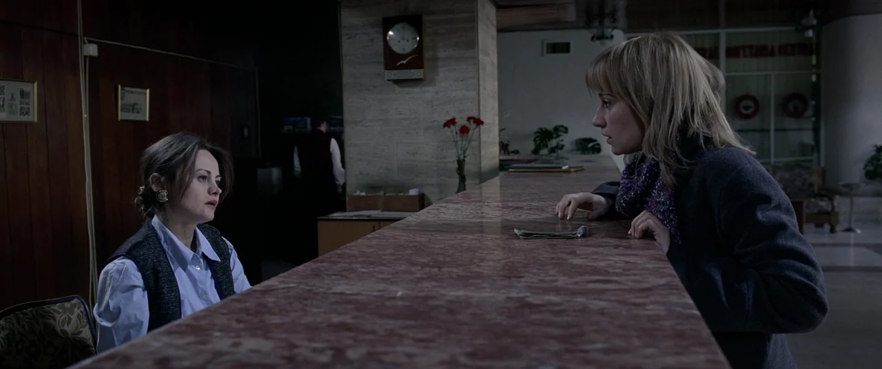 4 months, 3 Weeks and 2 Days (2007) movie still: medium — A hotel reception area with a polished red marble counter and wood-paneled walls. A female…