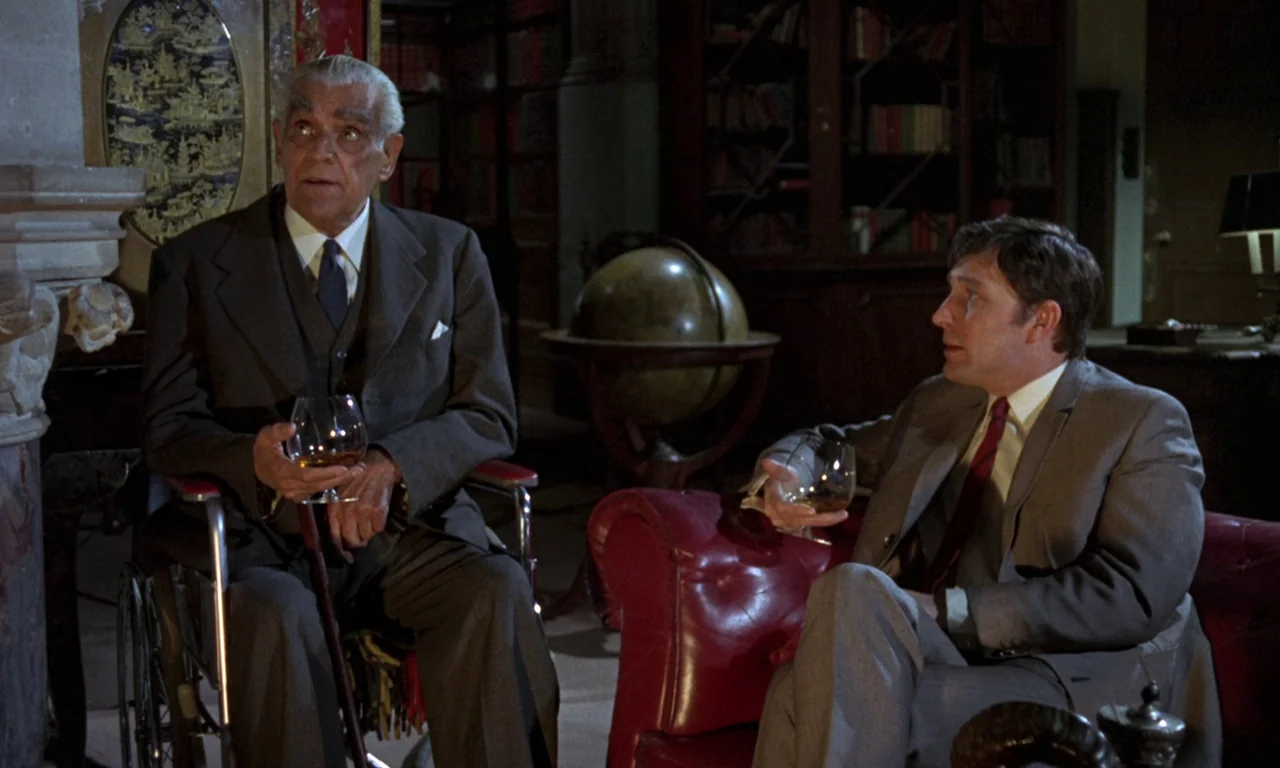 Curse of the Crimson Altar (1968) movie still: medium — A wood-paneled room containing a globe, a fireplace, and leather armchairs. Two men sit…