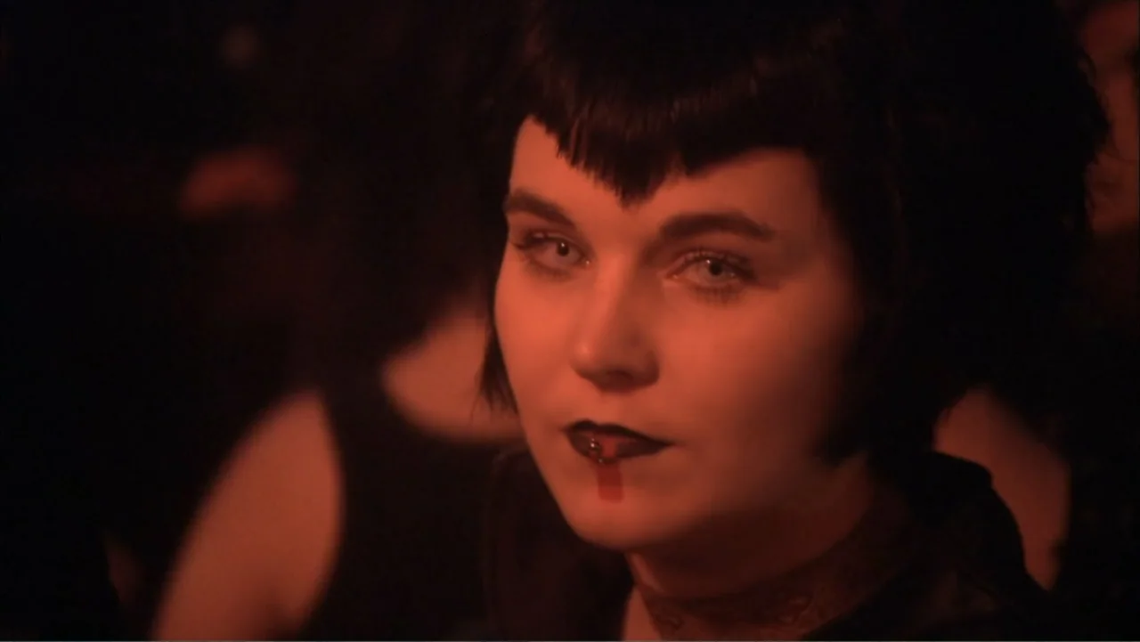 O código oculto (2025) movie still: closeup — A dimly lit club interior features a person positioned in the foreground. A young woman with short…