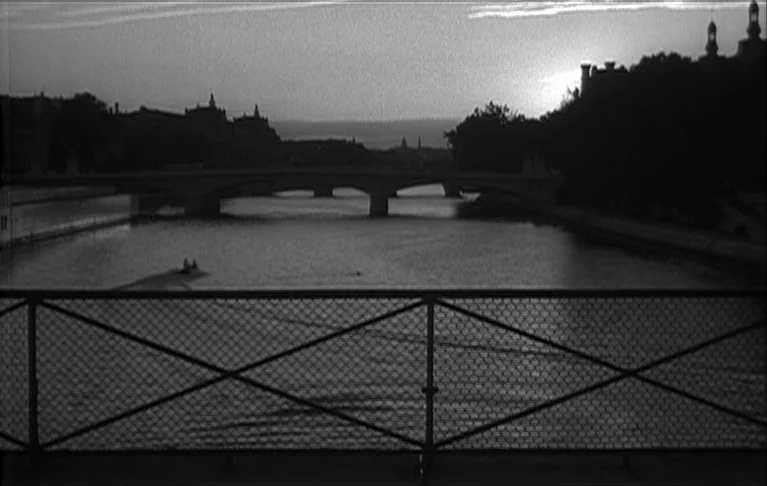 Le Signe du Lion (1962) movie still: wide — A wide view of a river in a city during the evening twilight. The Seine river flows under a stone bridge…