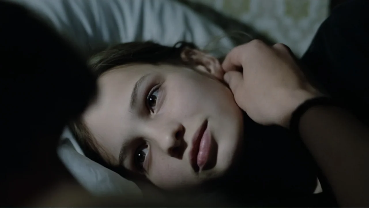 Christiane F. (1981) movie still: closeup — A dimly lit room focuses on a young girl lying on a white pillow. An adult hand enters the frame from…