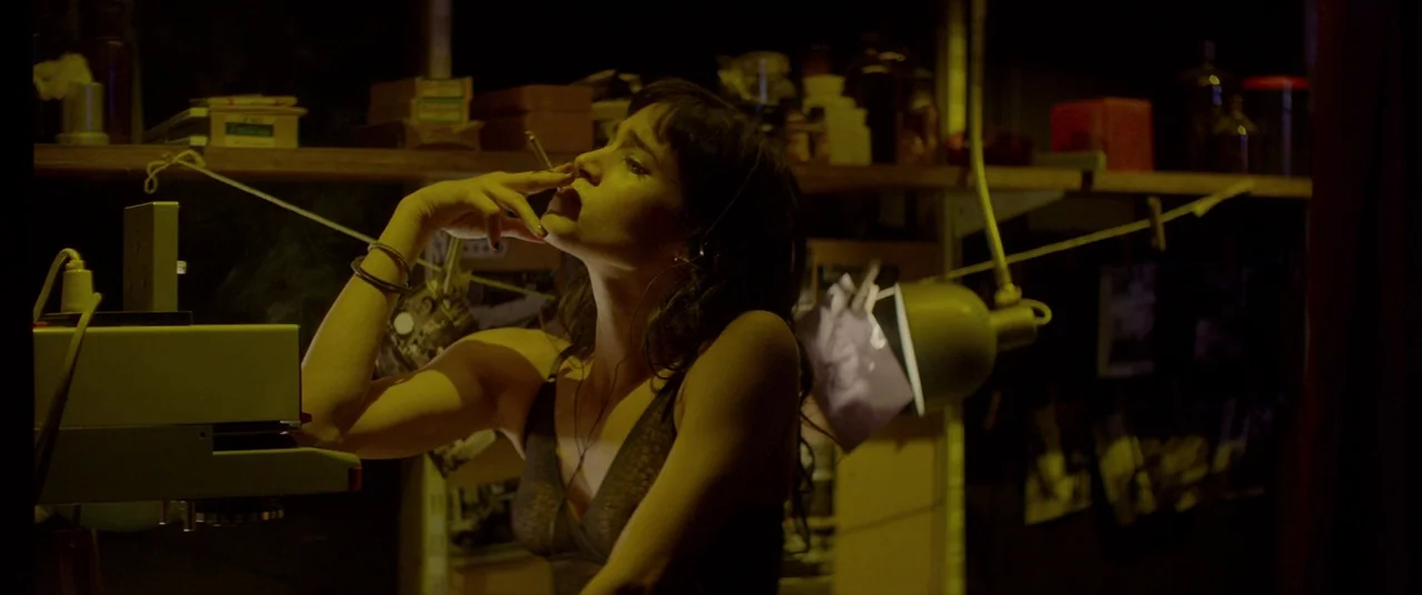 Atomic Blonde (2017) movie still: medium — A dimly lit photographic darkroom contains cluttered shelves with bottles and boxes. A young woman with…