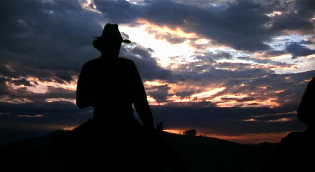 The Hired Hand (1971) movie still: medium — A dark silhouette of a person on horseback is positioned against a cloudy sunset. The rider in a cowboy…
