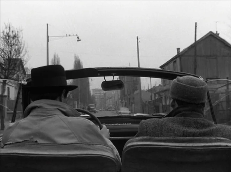 Band of Outsiders (Bande à part) (1964) movie still: medium — A view from the back seat of a convertible car moving down a street. Two men sit in…