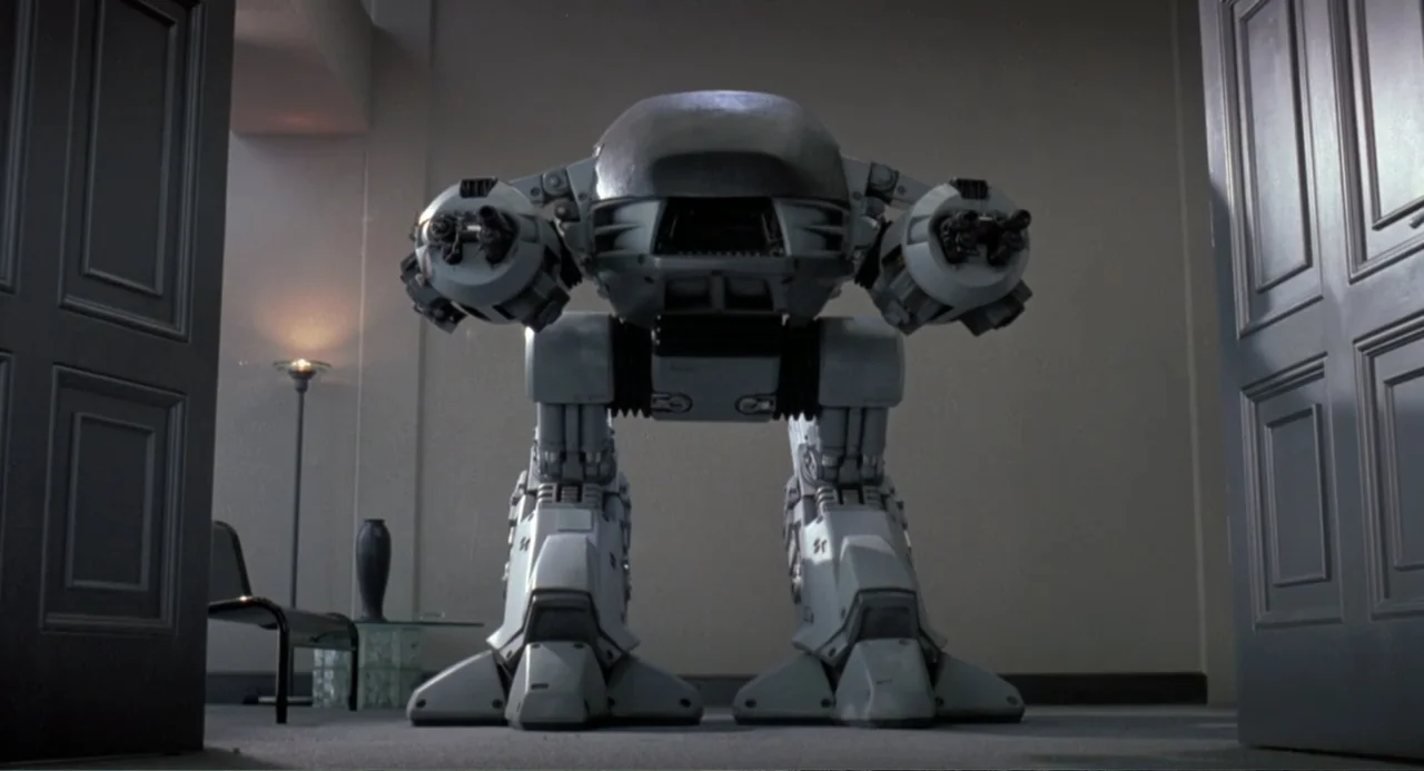 RoboCop (2014) movie still: fullbody — A spacious professional room features light walls and dual open doors at the entrance. A large bipedal robot…