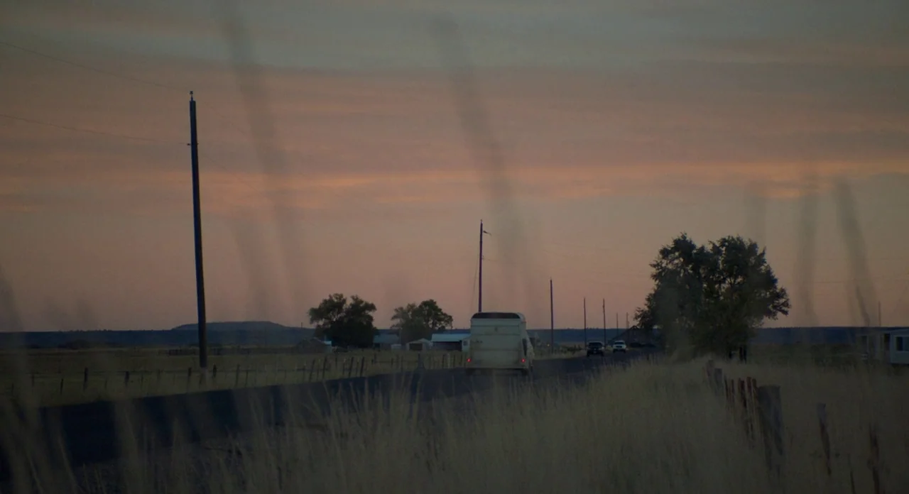 Lean on Pete (2017) movie still: wide — A quiet rural road stretches through dry grasslands at dusk under a fading sky. A single white vehicle moves…