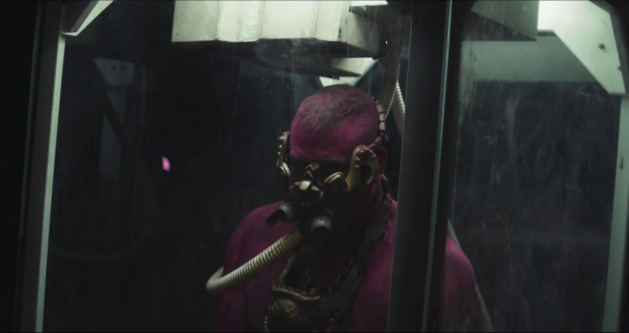 Prospect (2018) movie still: medium — A figure with bright magenta skin stands inside a small, glass-walled cylindrical container. The subject is…