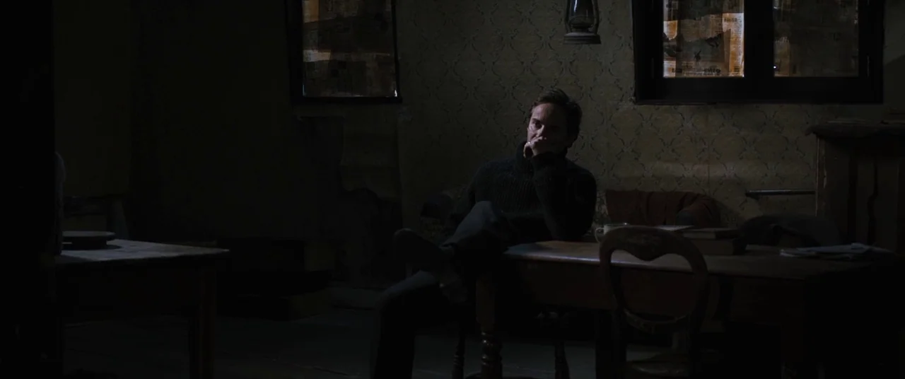Ginger & Rosa (2012) movie still: medium — A dimly lit room features patterned wallpaper and antique wooden furniture. A solitary man sits at a…