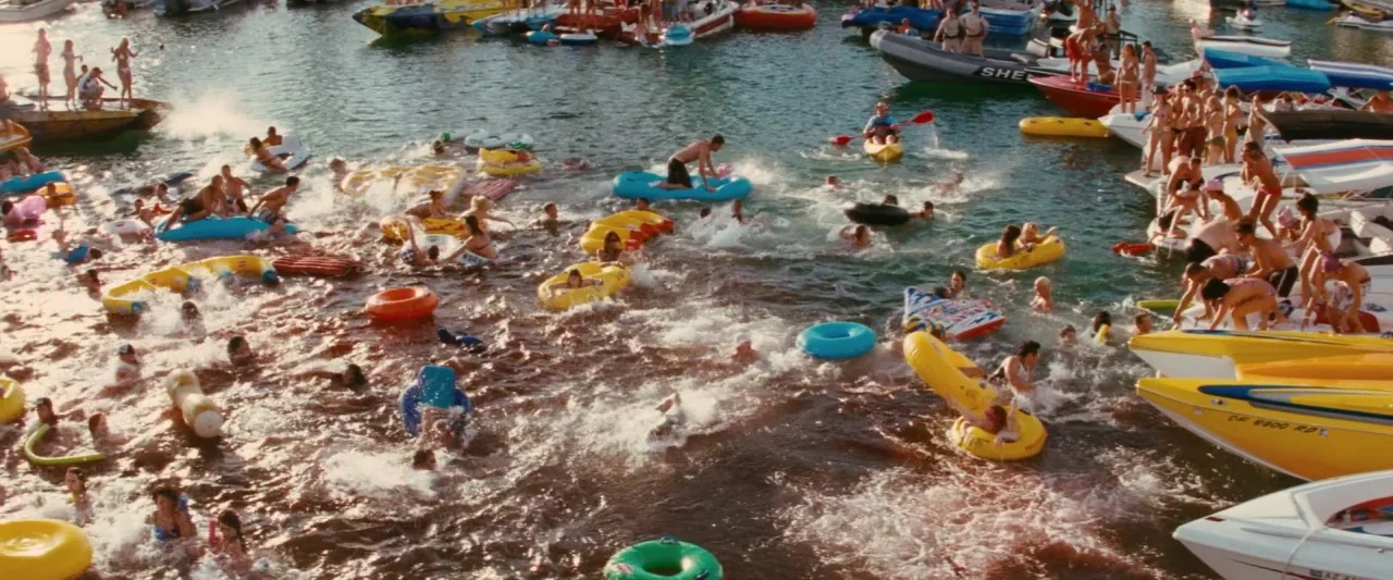 Piranha 3D (2010) movie still: wide — A crowded lake filled with people on colorful inflatable tubes and various motorboats. The water is churned by…