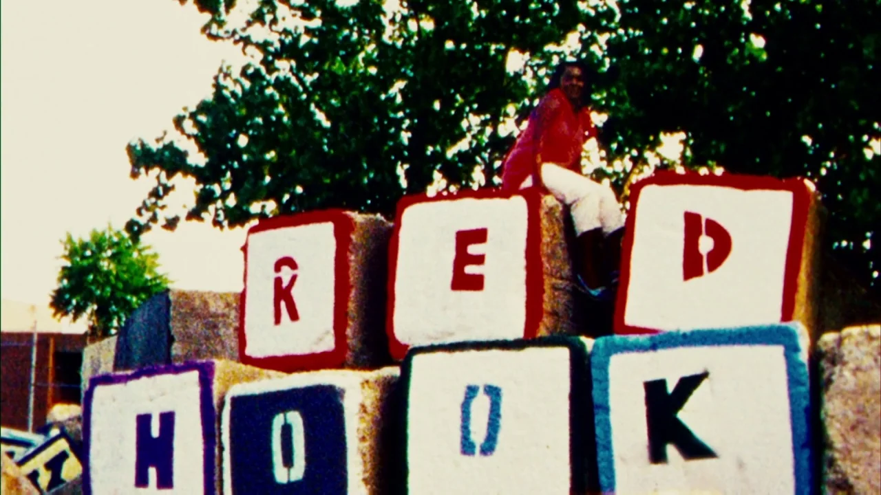 Red Hook Summer (2012) movie still: medium — A woman sits atop a structure of large white blocks painted with red letters. The background features…