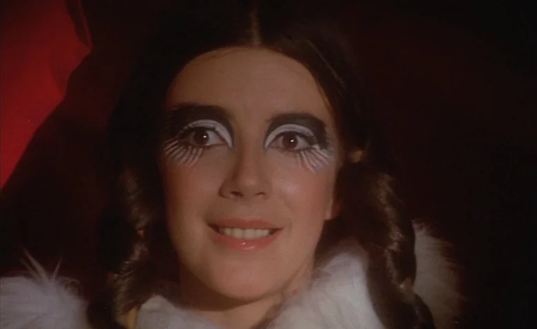 Sweet Movie (1974) movie still: closeup — A close portrait shows a woman against a dark, featureless backdrop. She wears elaborate stylized eye…