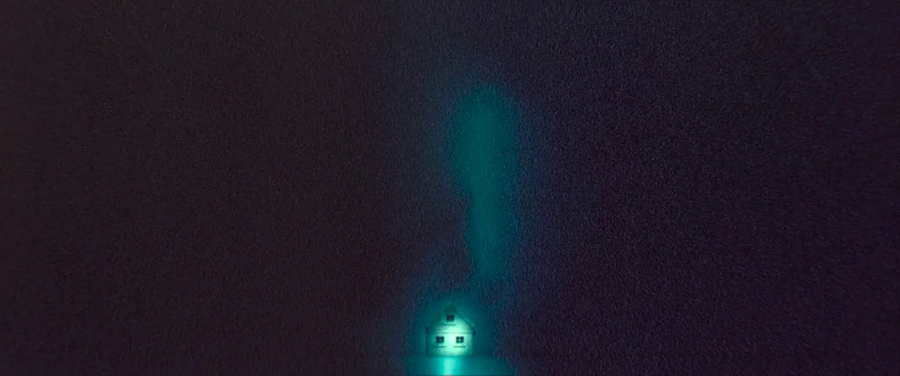 Skinamarink (2022) movie still: wide — A dark, textured expanse of land surrounds a tiny, glowing house at the bottom center. The small structure…