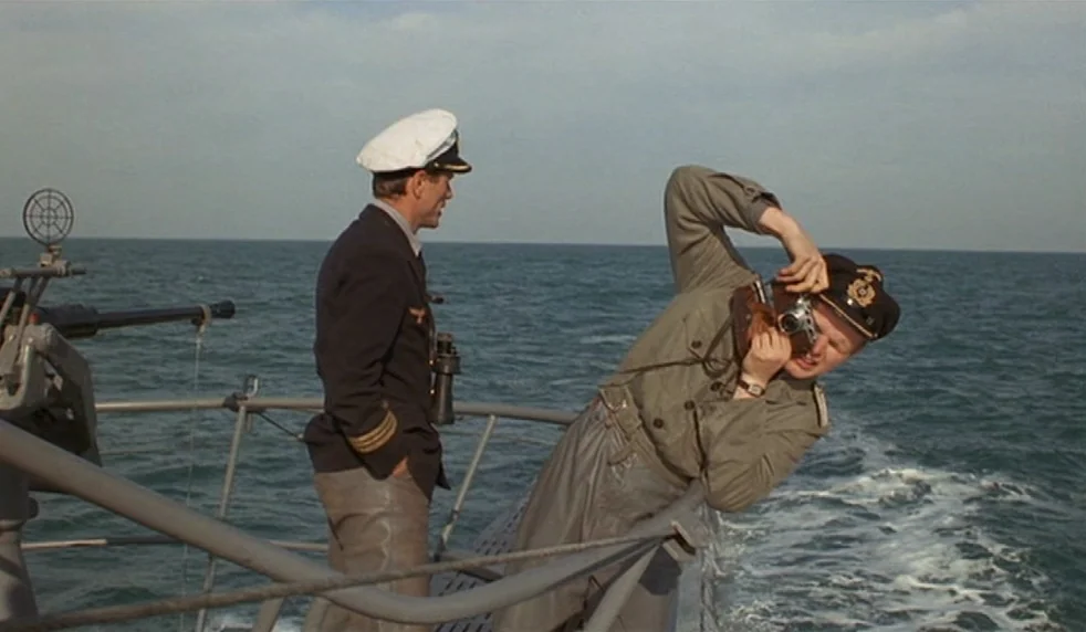 Das Boot (1981) movie still: medium — The deck of a submarine moving through open sea under a bright, overcast sky. One sailor leans over the…