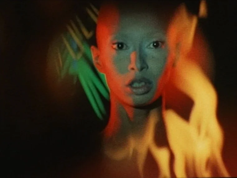 Salome (1972) movie still: closeup — A dark space provides a stark background for a close-up portrait of a woman. A flickering orange flame…
